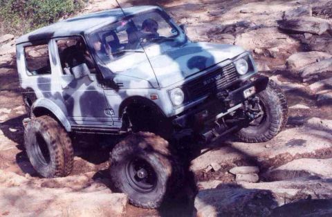 1989 Ford Bronco - Suzuki Samurai navigates a challenging rocky trail with large tires.