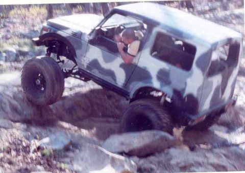 1989 Ford Bronco - A Suzuki Samurai navigates a rocky off-road course, with one wheel lifted high.