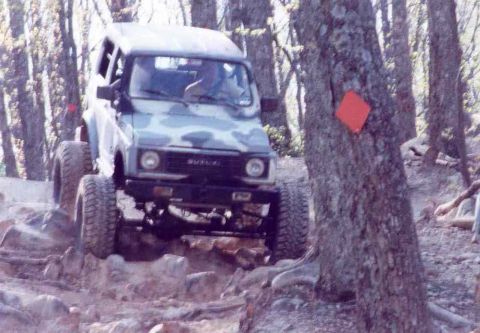 1989 Ford Bronco - Suzuki Samurai navigates a challenging rocky trail in a wooded area.