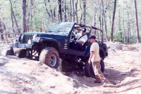 1989 Ford Bronco - A dark green Jeep Wrangler navigates a rocky off-road trail with two individuals observing.