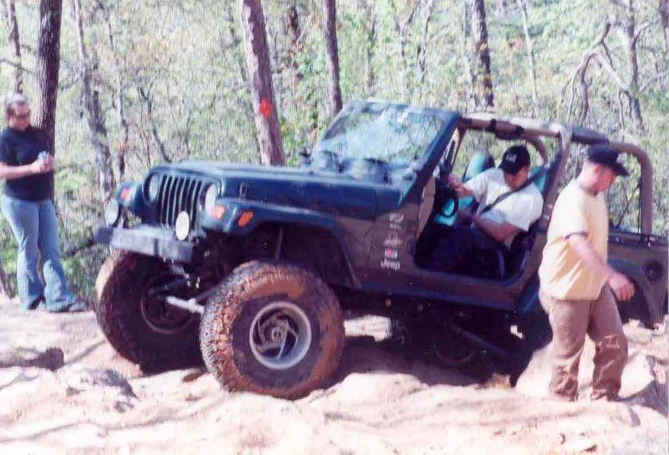 Dark green Jeep Wrangler on a dirt trail with two people nearby
