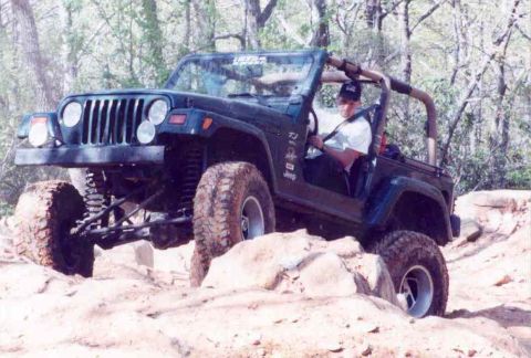 1989 Ford Bronco - A driver navigates a Jeep Wrangler over a rocky, off-road trail.