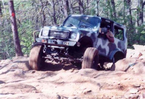 1989 Ford Bronco - A Suzuki Samurai navigates a challenging rocky trail with its front-left wheel high in the air.
