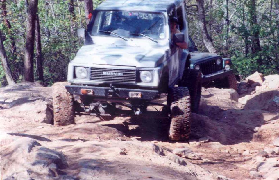 Suzuki Samurai on rocky terrain, front view, camouflage paint