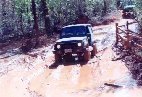 1989 Ford Bronco - A Suzuki Samurai navigates a muddy off-road trail with another vehicle in the distance.
