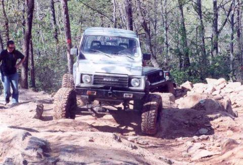 1989 Ford Bronco - A Suzuki Samurai navigates a challenging rocky terrain with a person standing nearby.