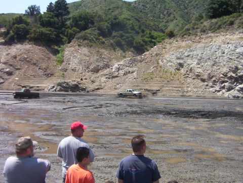 2000 Ford F-450 - Trucks navigate a muddy terrain in a scenic, hilly landscape.