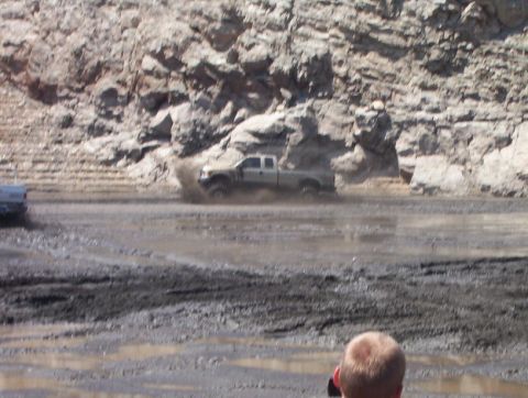 2000 Ford F-450 - Two trucks navigate a muddy terrain with a rocky cliff face in the background.
