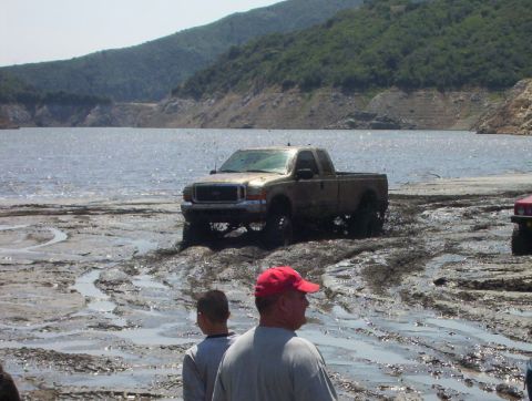 2000 Ford F-450 - Gold 2000 Ford F-450 truck stuck in mud near a lake, with another vehicle visible to the right.