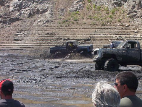 2000 Ford F-450 - Several trucks are navigating a challenging muddy landscape, with onlookers observing the event.