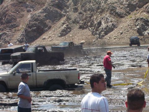 2000 Ford F-450 - Multiple trucks are bogged down in a muddy area, with onlookers observing the scene.