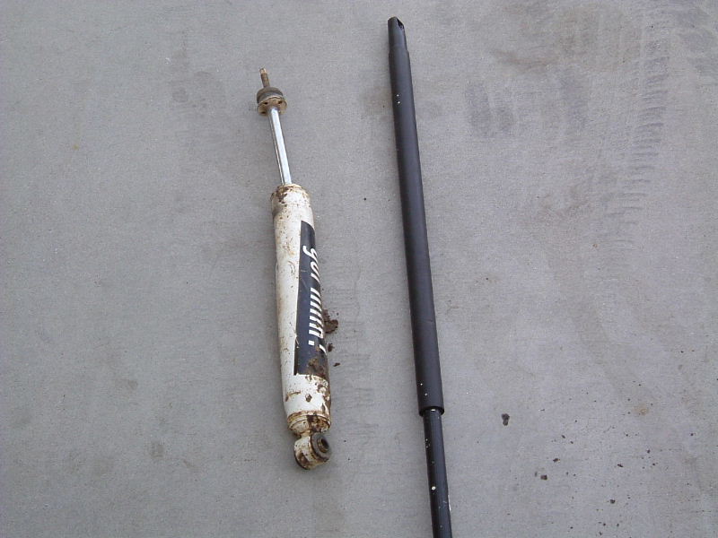 White used shock absorber and a black metal tube lying on a concrete floor