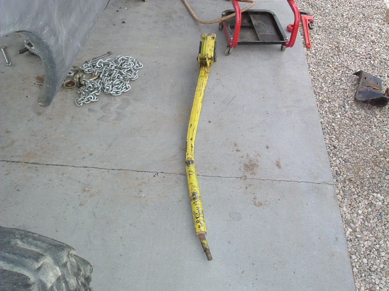 Bent yellow steel bar on a concrete pad with tow chains and a red engine stand nearby