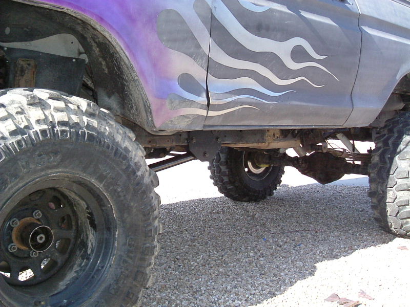 Lifted truck on mud tires with purple flame paint, viewed low along the rocker and axle