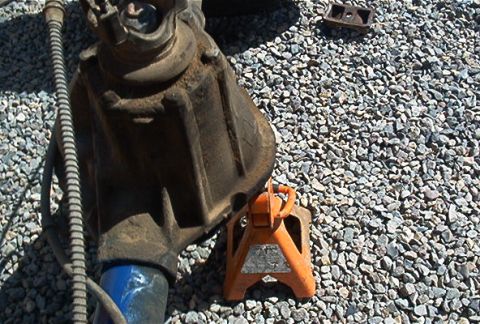 1986 Ford Bronco - A vehicle's differential is shown resting on an orange jack stand on a bed of gravel.