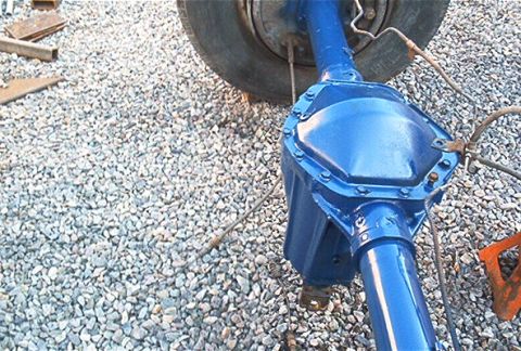 1986 Ford Bronco - A close-up view of a blue painted rear axle assembly, likely from a truck or SUV, on a gravel surface.