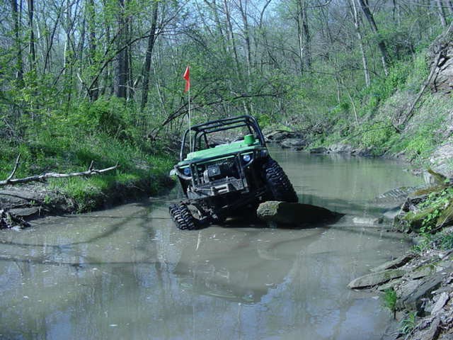 Green off-road vehicle in stream with orange flag