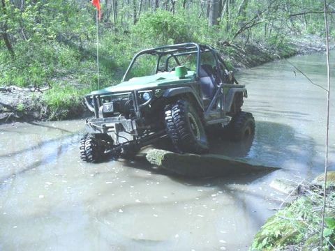 1992 Ford Bronco - Off-road vehicle navigates a stream with a flag on a pole in the background.