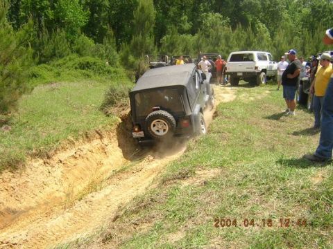 2002 Jeep Wrangler - A group of Jeeps and other vehicles are gathered off-road, with one Jeep tackling a challenging dirt path.