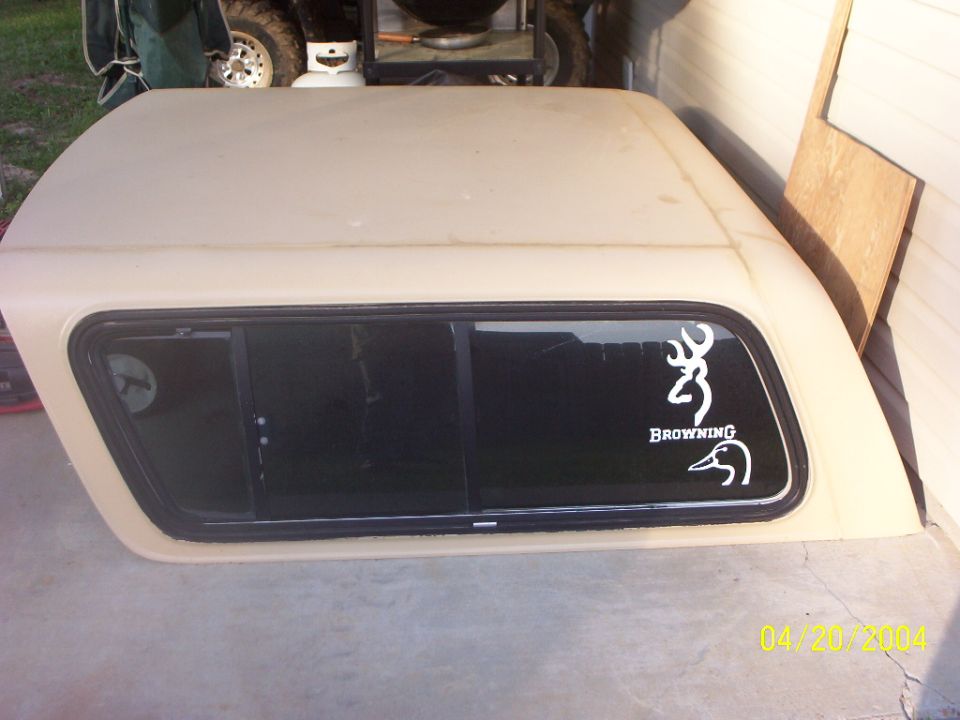 Tan fiberglass truck canopy with sliding window and Browning buck decal in a garage