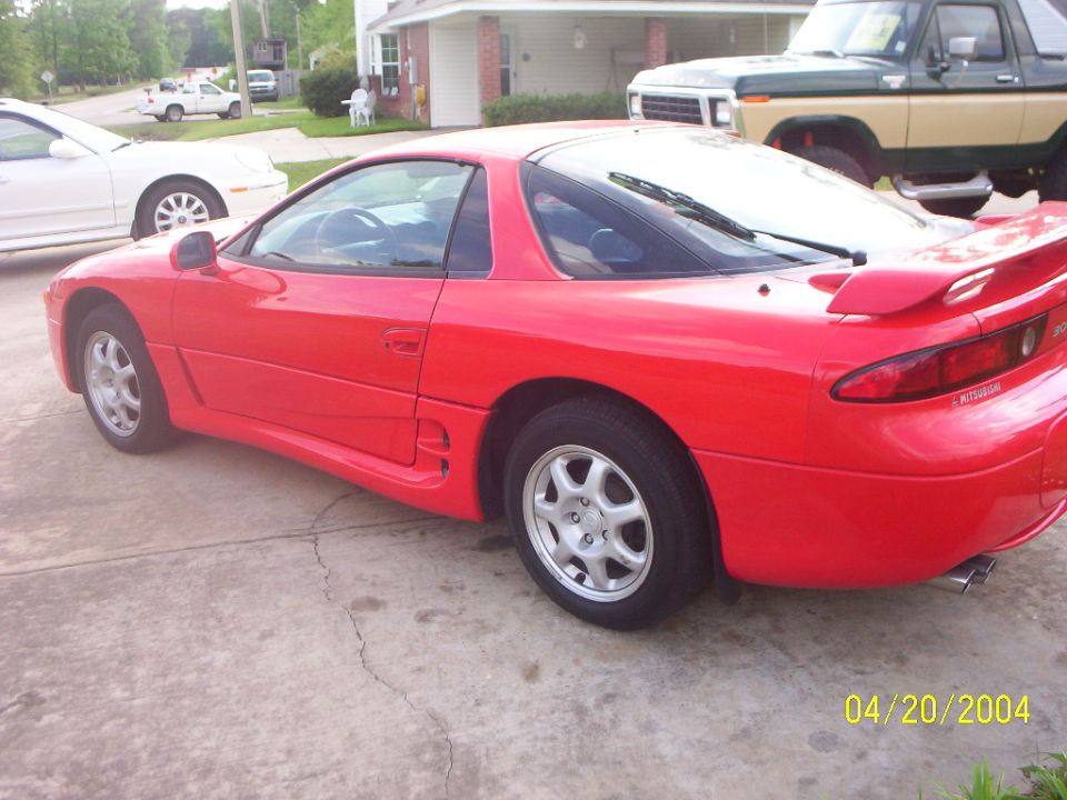 Red Mitsubishi 3000GT coupe parked on driveway, rear three-quarter view with rear spoiler