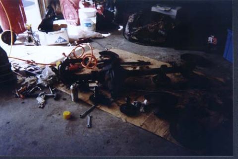 1996 Ford Bronco - A bare axle housing lies across cardboard on a garage floor with a coiled orange air hose, a hub assembly and hand tools spread around it.…