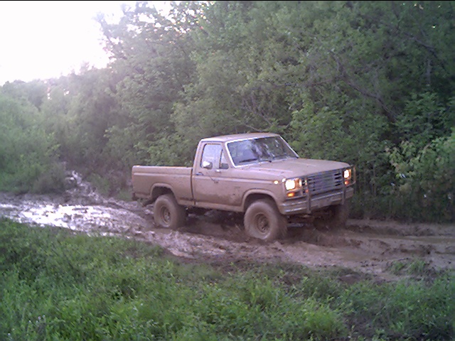Tan Ford 4x4 pickup with brush guard sitting in a muddy trail, front quarter view