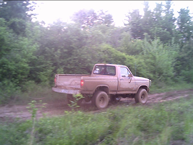 Tan pickup truck driving away on a muddy trail, rear quarter view at dusk