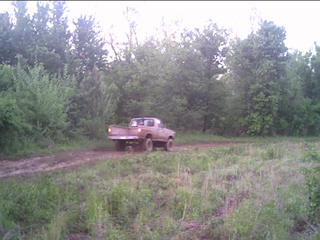 Pickup truck on a dirt clearing surrounded by green woods in dim evening light