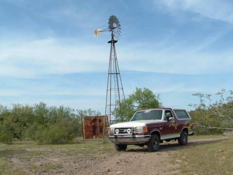 1990 Ford Bronco - A 1990 Ford Bronco sits parked on a dirt road with a windmill in the background.