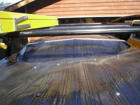 1978 Ford Bronco - A tarp is stretched over the roof of a vehicle, obscuring its details. A ladder rack is mounted above.