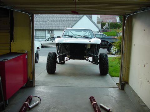 1981 Ford Bronco - Custom off-road truck chassis in garage, with other vehicles visible outside. Year is not determinable from image.