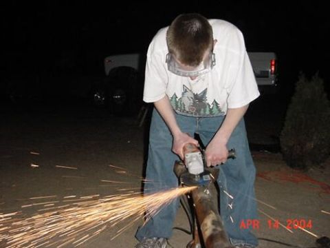 1996 Ford Bronco - Night shot of a person in safety glasses and a wolf-print T-shirt using an angle grinder on a rusty length of tube or axle housing, throwin…
