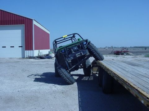 1992 Ford Bronco - A green off-road vehicle is precariously positioned on a flatbed trailer, with its tires angled on the edge.