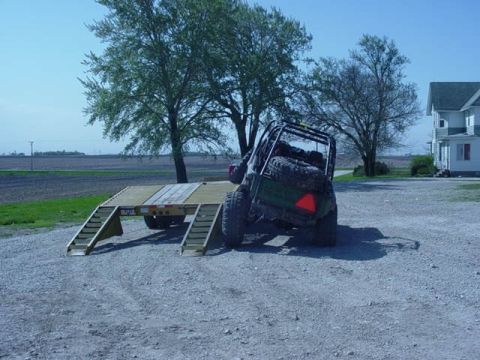 1992 Ford Bronco - Off-road vehicle loaded onto a trailer in a gravel lot with trees and a house in the background.