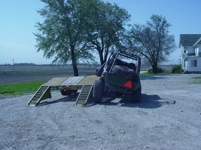 Green off-road vehicle with spare tire on back, parked on a trailer with ramps