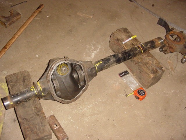 Ford Dana 44 axle housing with differential cover removed, resting on wooden blocks. Tape measure and other tools nearby