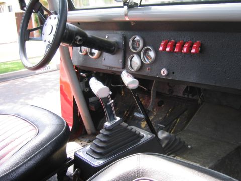 1969 Ford Bronco - The interior of a vehicle shows a custom steering wheel, multiple gauges, and two prominent gear shifters.