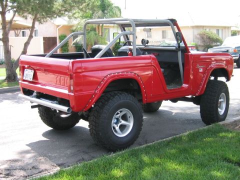 1969 Ford Bronco - This red 1969 Ford Bronco features a roll cage and off-road tires, seen from a rear 3/4 perspective.