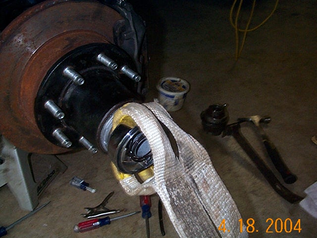 Rusty brake rotor and wheel hub with studs during hub removal, tools on garage floor.
