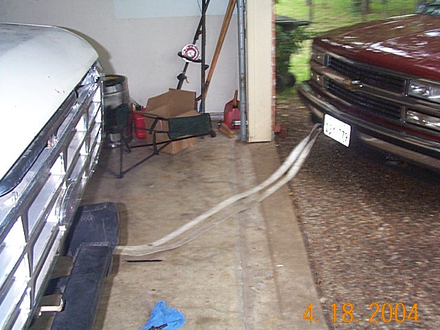 White vehicle grille and maroon Chevy pickup front end in carport with strap on floor