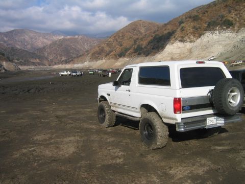 1993 Ford Bronco - A white 1993 Ford Bronco sits in a dusty, open area with mountains under a cloudy sky.