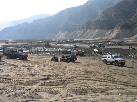 1993 Ford Bronco - Many vehicles, including trucks and ATVs, are parked and driving in a large, open, dry riverbed area.