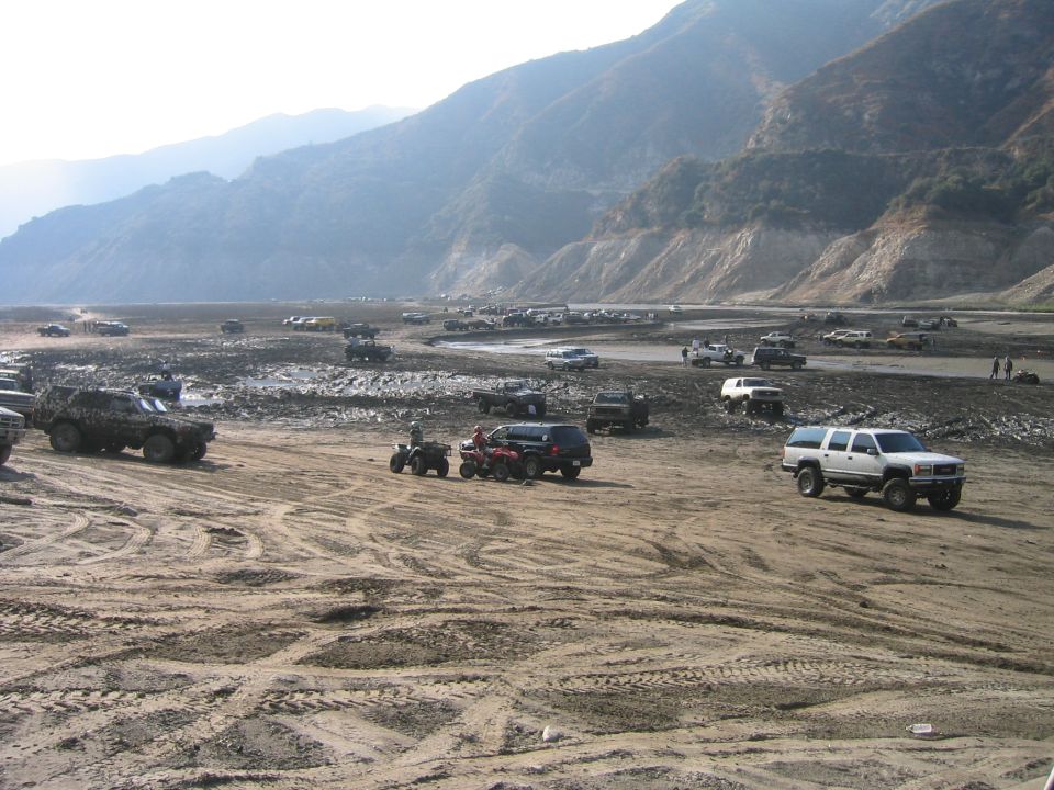 Off-road staging area in a dry riverbed with many 4x4 trucks, SUVs and ATVs