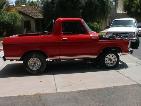 1979 Ford Bronco - Side view of a red 1979 Ford Bronco, hood open, with a white SUV in the background.