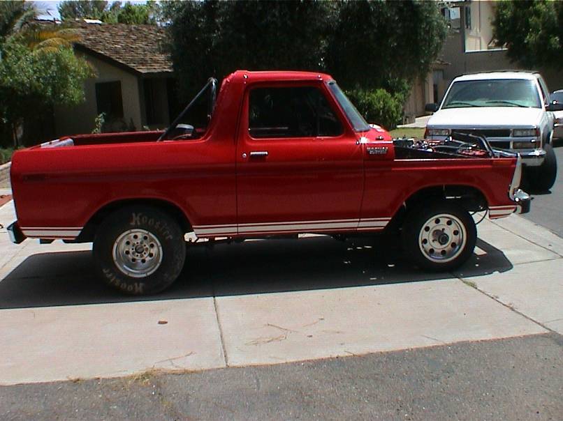 Red late-70s Ford Bronco drag build with top removed, roll bar, and Hoosier rear slicks in a driveway