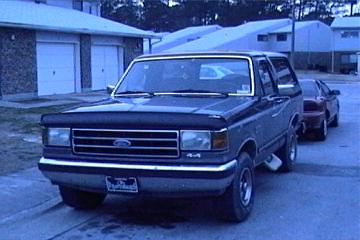 1989 Ford Bronco - 1989 Ford Bronco parked in front of residential garages with another vehicle behind it.