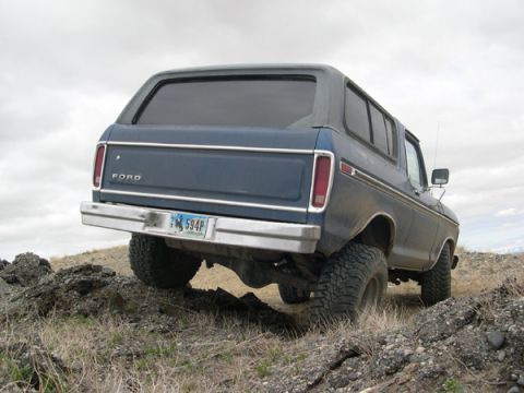 1978 Ford Bronco - Rear view of a blue 1978 Ford Bronco navigating off-road terrain with a chrome bumper and tinted windows.