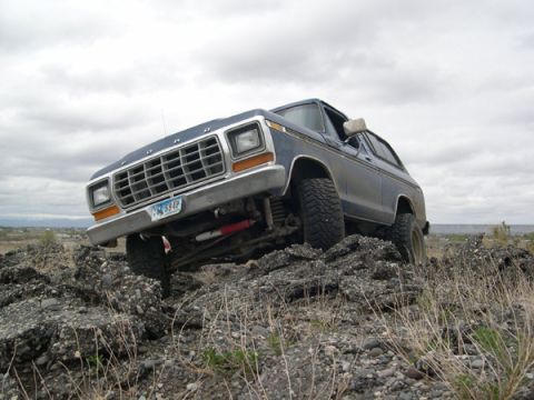 1978 Ford Bronco - A blue 1978 Ford Bronco navigates a rocky terrain under a cloudy sky.