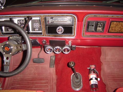 1978 Ford Bronco - Interior shot of a red dash and red carpet in a classic truck, with a woodgrain-trimmed dashboard, slide-lever HVAC controls, an aftermarke…